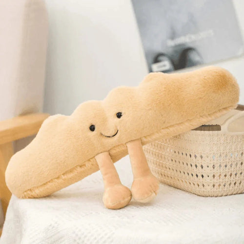 Beige baguette plush toy with embroidered smiling face and dangling fabric limbs resting on white surface