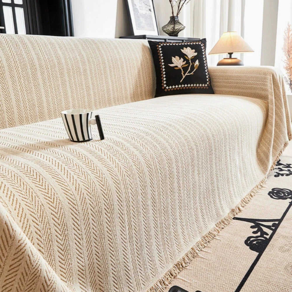 Beige herringbone chenille sofa throw draped over neutral sofa with tasselled fringe edges and textured knit weave