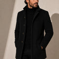 Men's tailored coat with stand collar and button-front closure in solid black worn over turtleneck