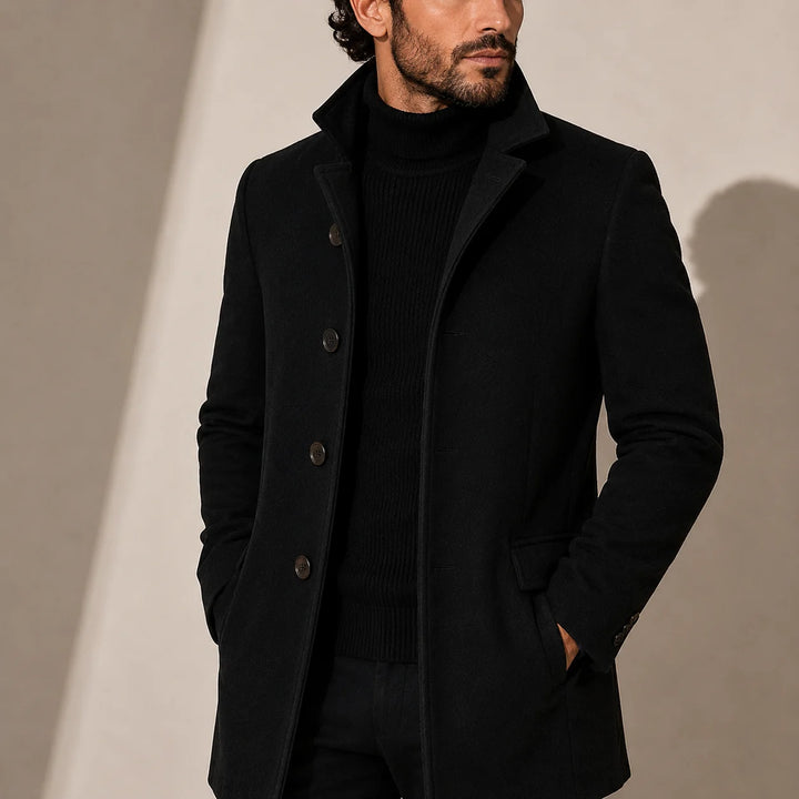Men's tailored coat with stand collar and button-front closure in solid black worn over turtleneck