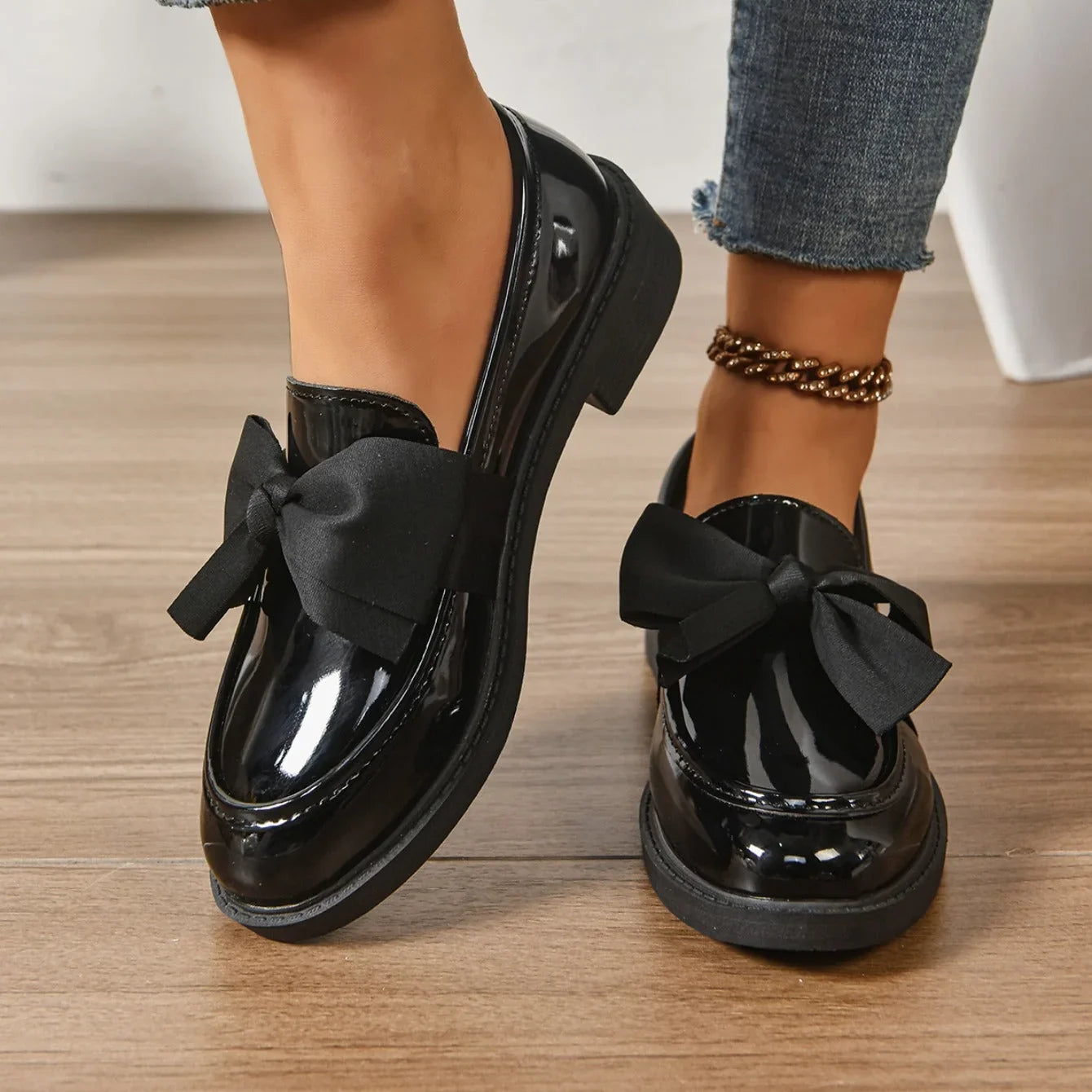 Patent loafers with bow detail worn with tailored trousers on model