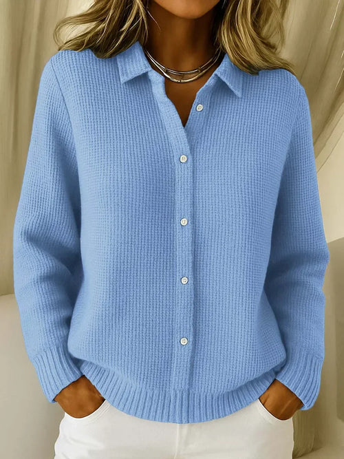 Woman wearing blue collared knit cardigan with button-through front and ribbed texture over white trousers