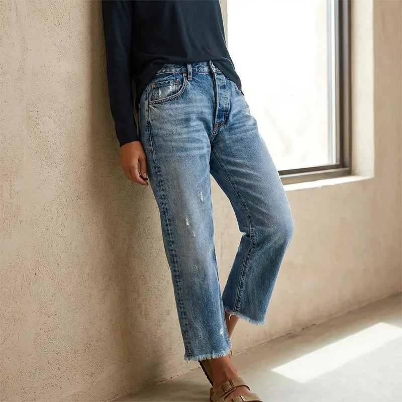 Side detail of distressed denim jeans with faded wash and raw hem finish