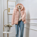 Women's cropped hooded puffer jacket in peach displayed on hanger with beige jumper and jeans