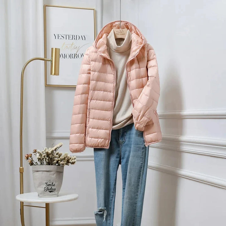 Women's cropped hooded puffer jacket in peach displayed on hanger with beige jumper and jeans