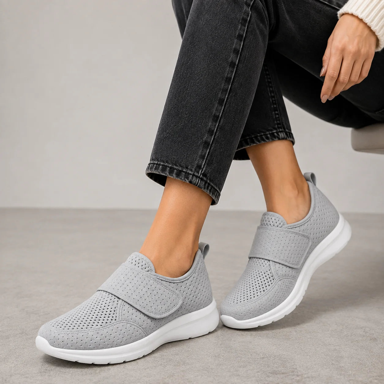 Woman wearing grey wide fit trainers with adjustable strap and perforated upper paired with black cropped trousers