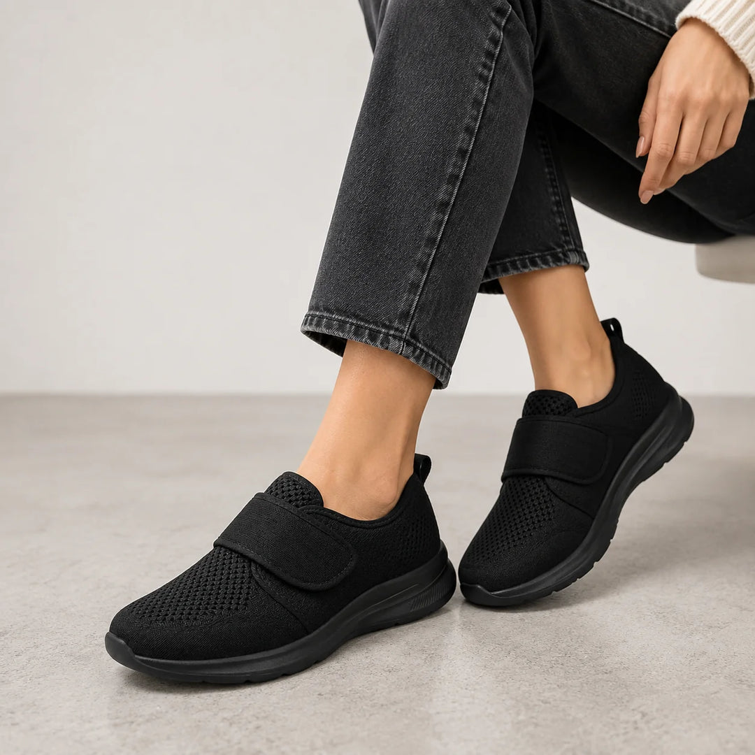 Woman's feet in grey perforated trainers with adjustable strap, styled with casual black trousers