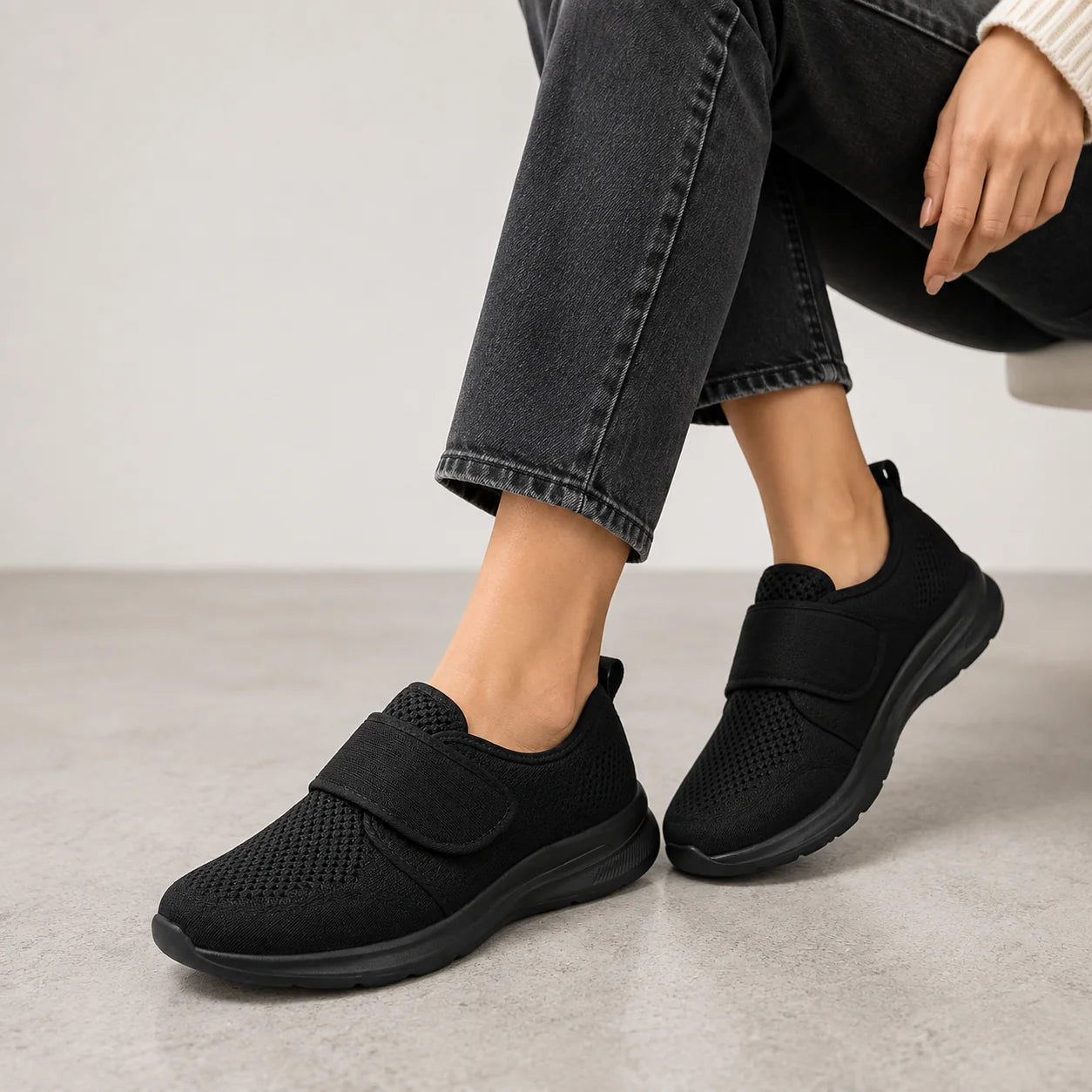 Woman's feet in grey perforated trainers with adjustable strap, styled with casual black trousers