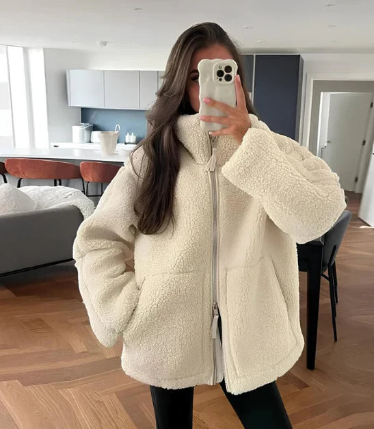 Woman wearing a cream oversized teddy fleece jacket with full zip closure and funnel neck