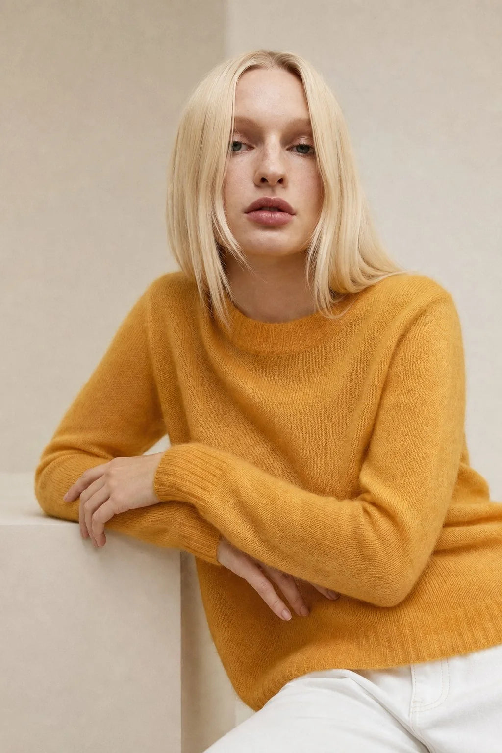 Woman wearing a mustard yellow women's mohair crewneck jumper with relaxed fit and ribbed cuffs paired with white trousers