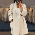Woman wearing beige oversized knit cardigan with open front and deep pockets over white top