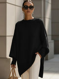 Woman wearing a women's oversized jumper with asymmetric hem in black, paired with cream trousers and sunglasses