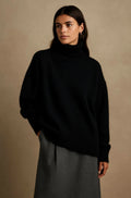 Woman wearing oversized black turtleneck jumper with relaxed fit and ribbed cuffs styled with grey skirt