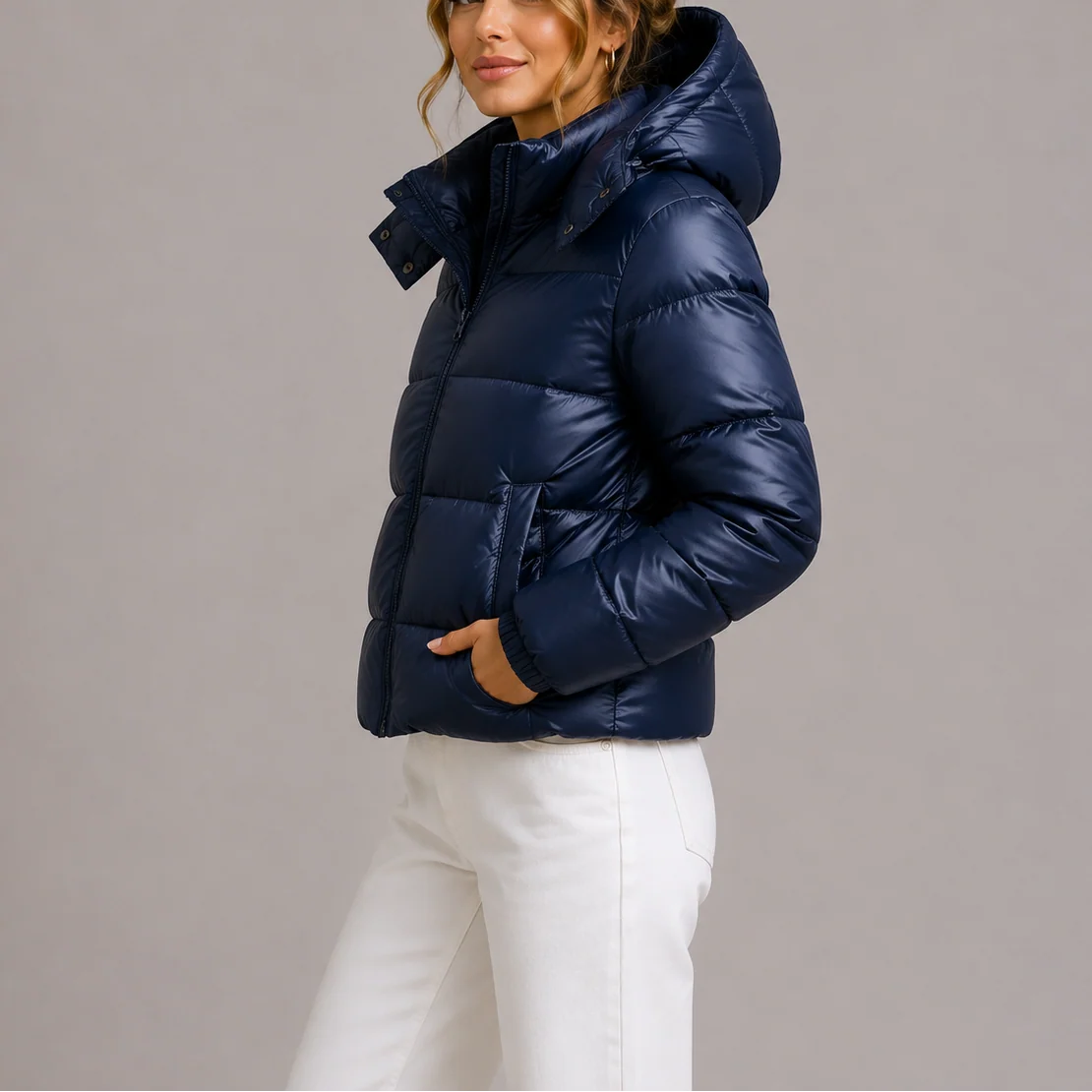 Woman wearing navy hooded puffer jacket with quilted design and cropped fit over white trousers