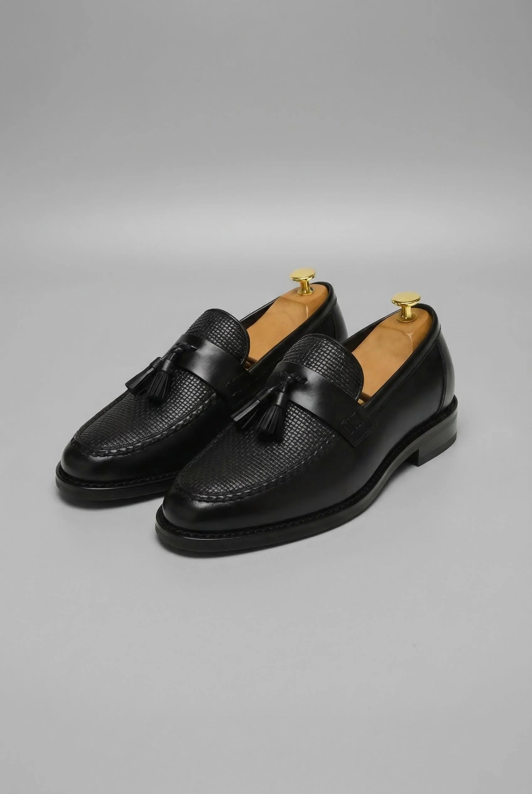 Men's tassel loafers in black with woven vamp detail and slip-on design on neutral background