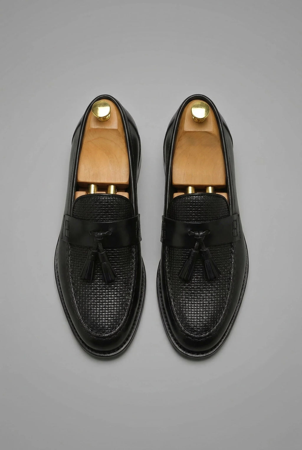 Close-up view of men's black tassel loafers showing textured woven vamp and smooth strap