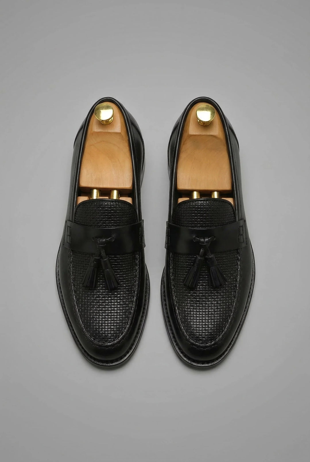 Close-up view of men's black tassel loafers showing textured woven vamp and smooth strap