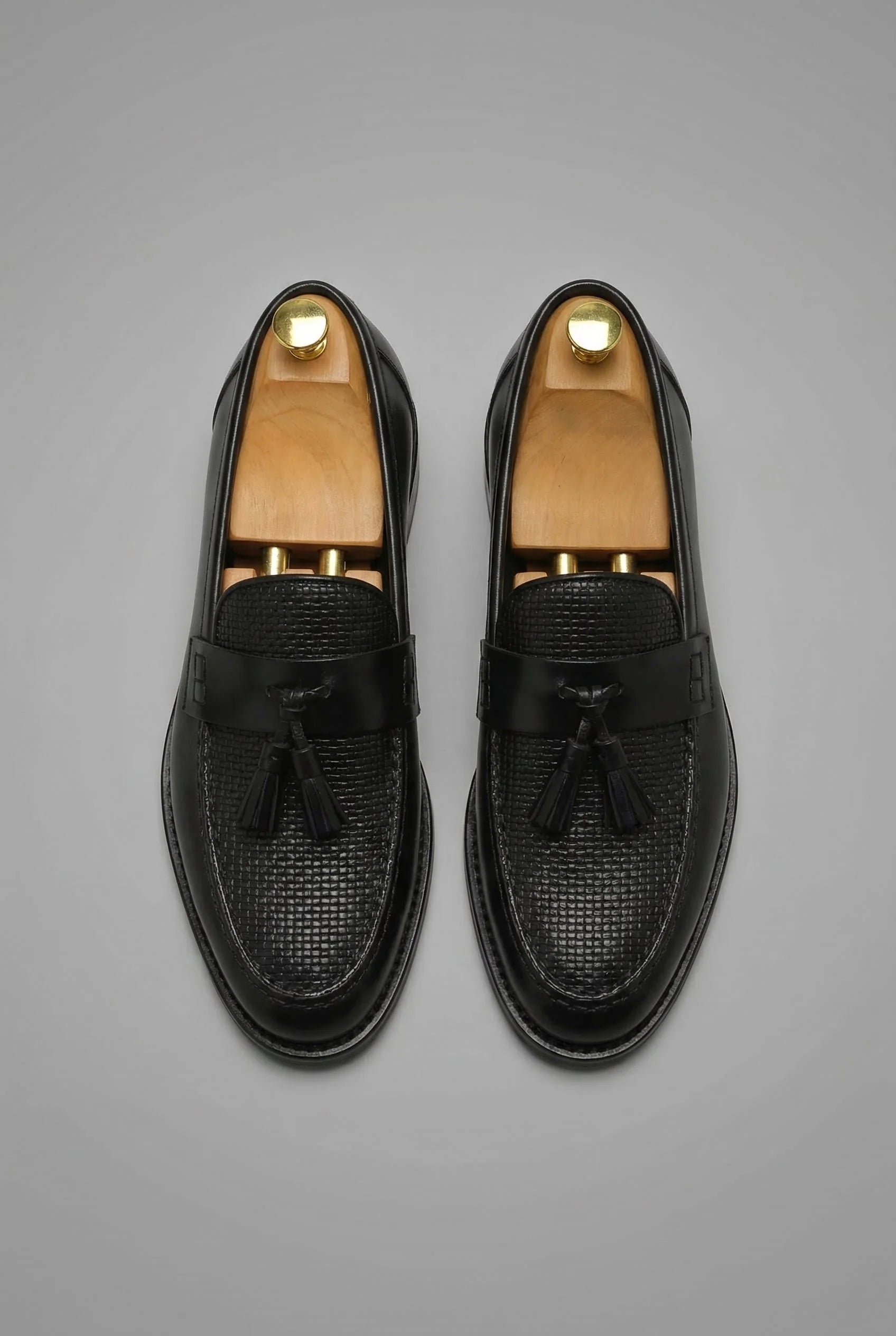 Close-up view of men's black tassel loafers showing textured woven vamp and smooth strap