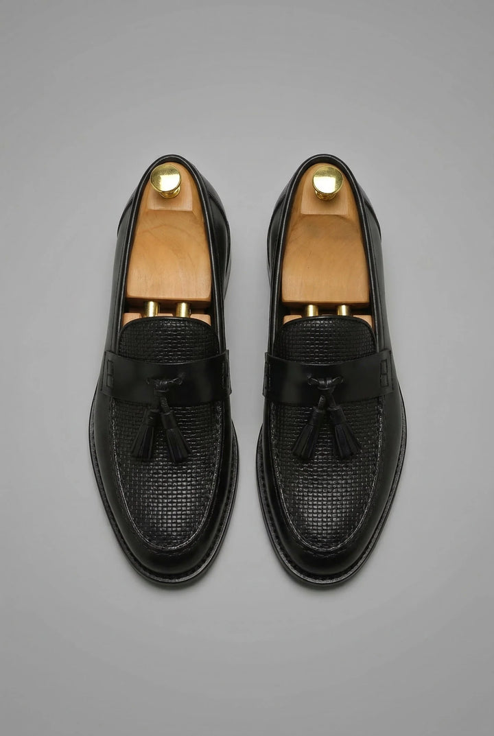 Close-up view of men's black tassel loafers showing textured woven vamp and smooth strap