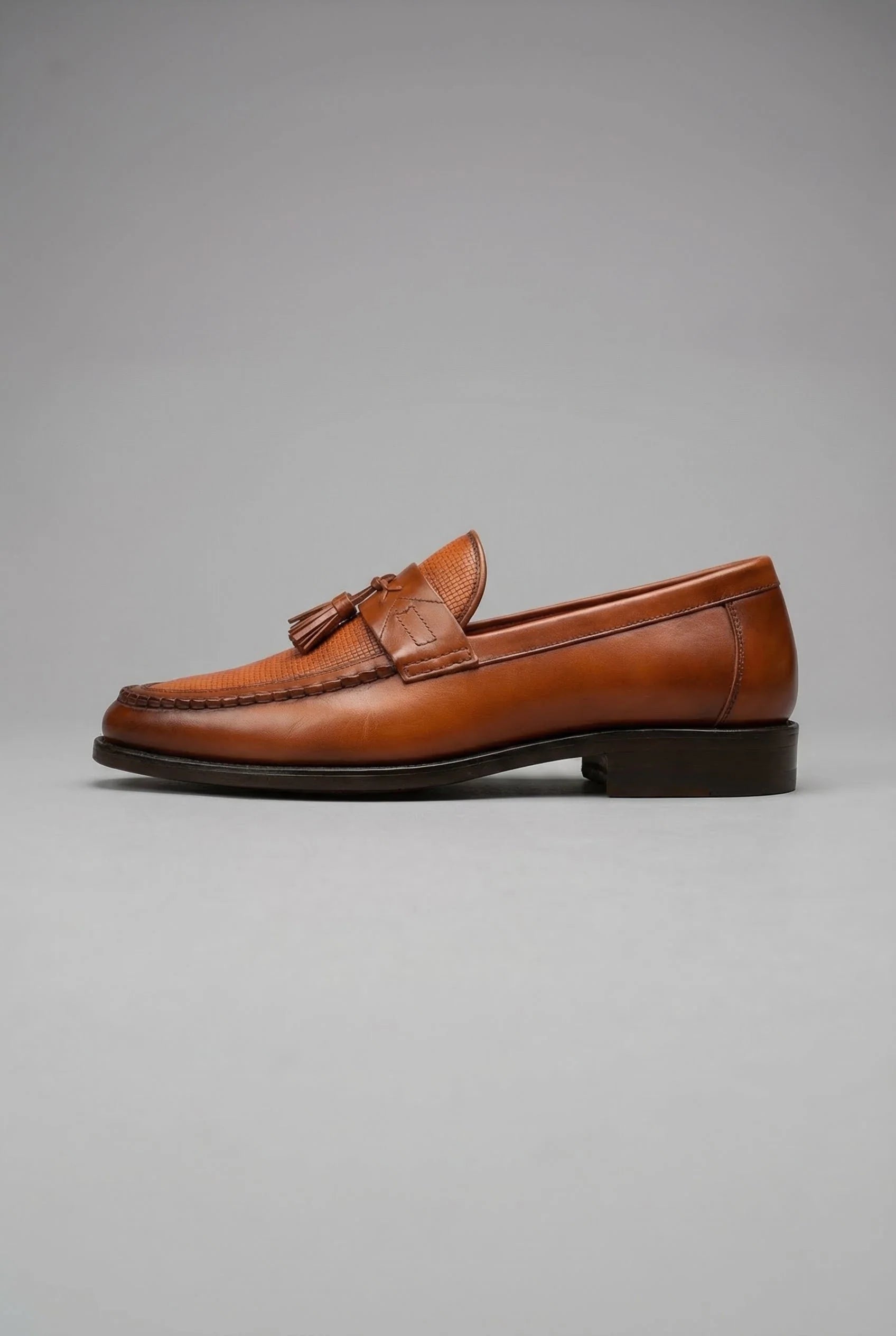Men's black tassel loafers displayed from three-quarter angle highlighting refined finish