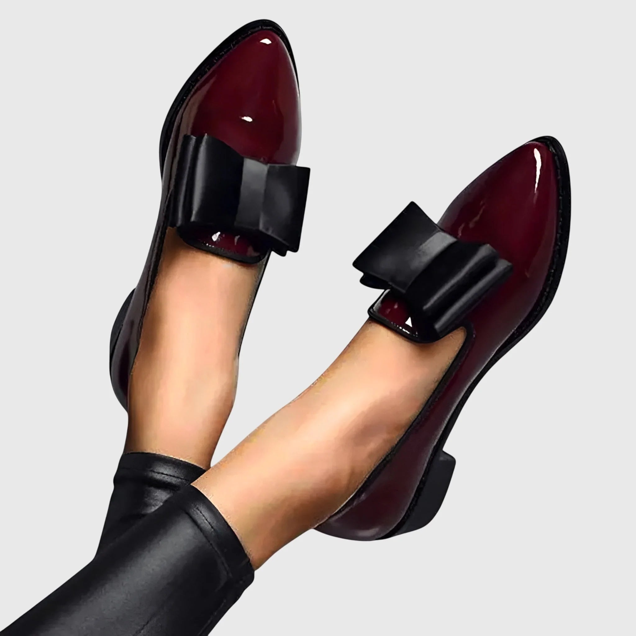 Women's patent loafers in burgundy with black bow detail and pointed toe on model feet