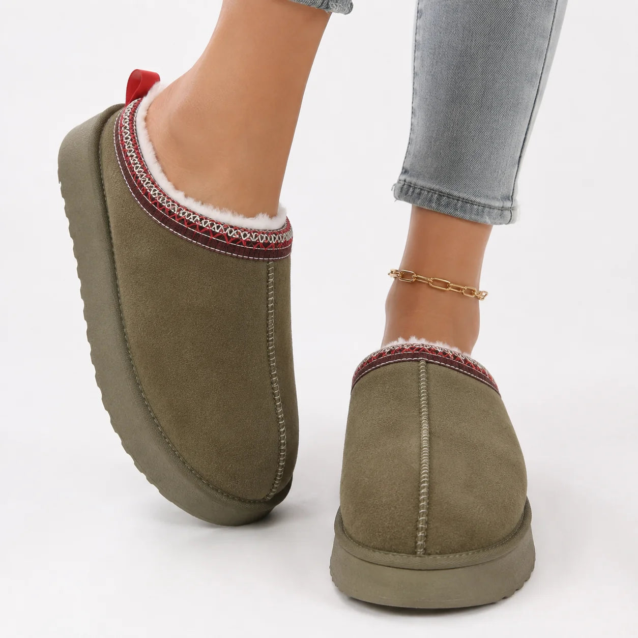 Women's faux suede slippers in olive with fleece lining and decorative woven trim worn with grey jeans