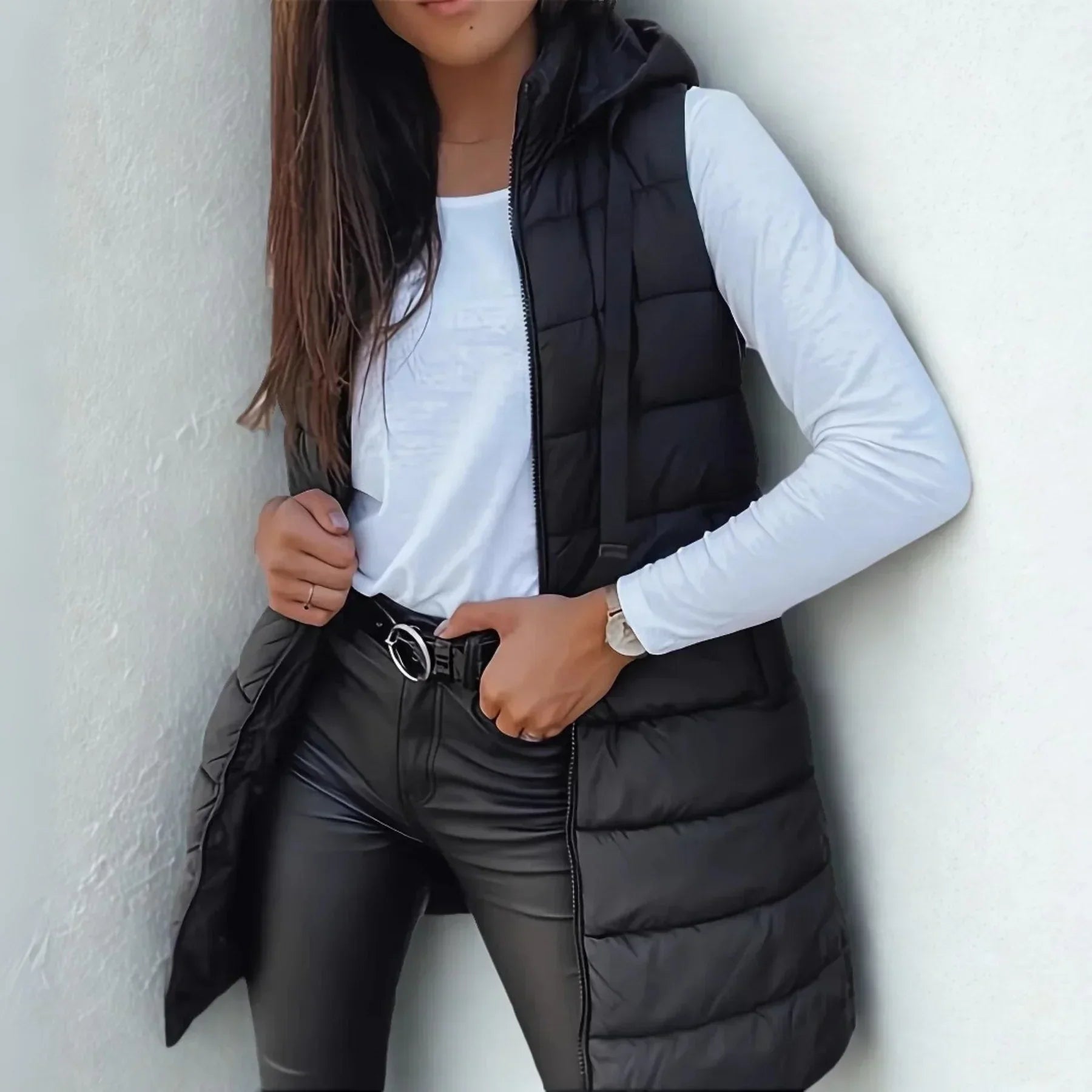 Women's long puffer gilet in black with hooded neckline and full-length zip closure worn over white top