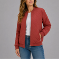 Woman wearing a terracotta quilted bomber jacket with diamond stitching and ribbed cuffs, paired with jeans