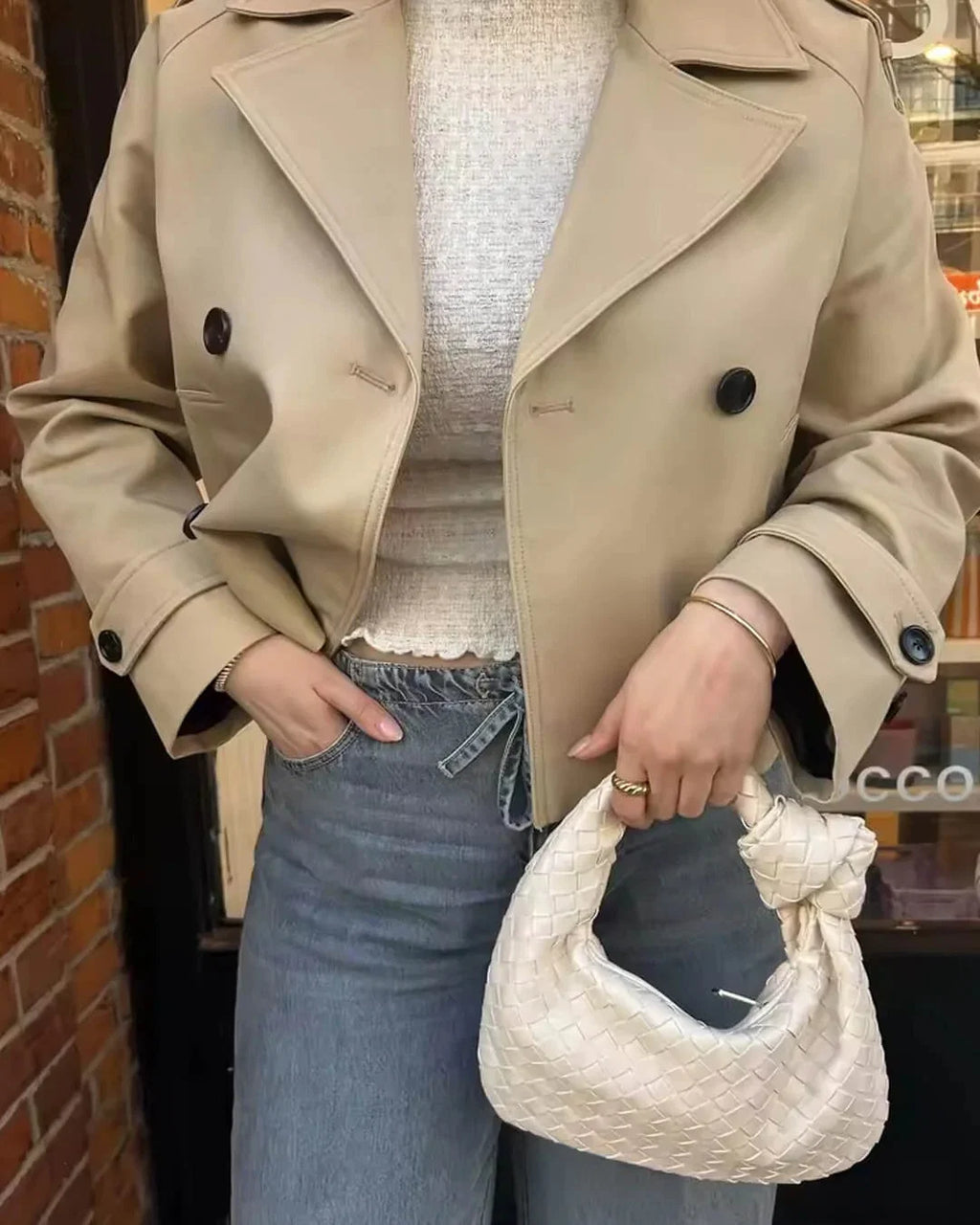 Detail of double-breasted button closure on women's cropped trench jacket
