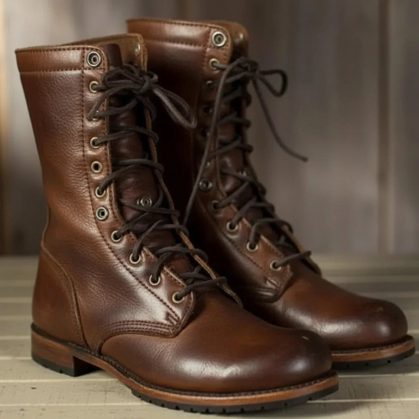 Women's lace-up mid-calf boots in brown with metal eyelets and flat sole on wooden floor