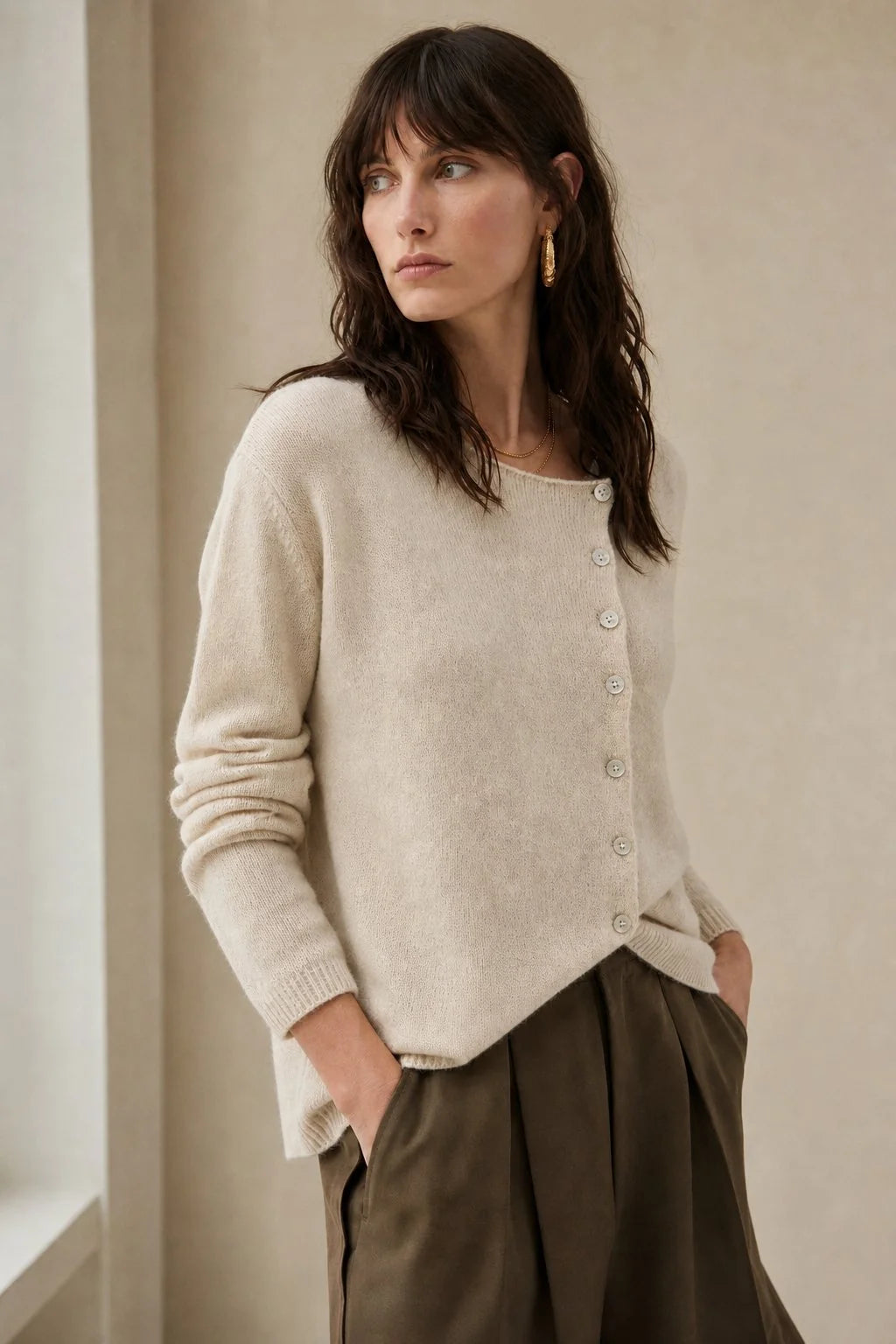 Model wearing a beige women's cashmere cardigan with asymmetric button detail and relaxed fit silhouette