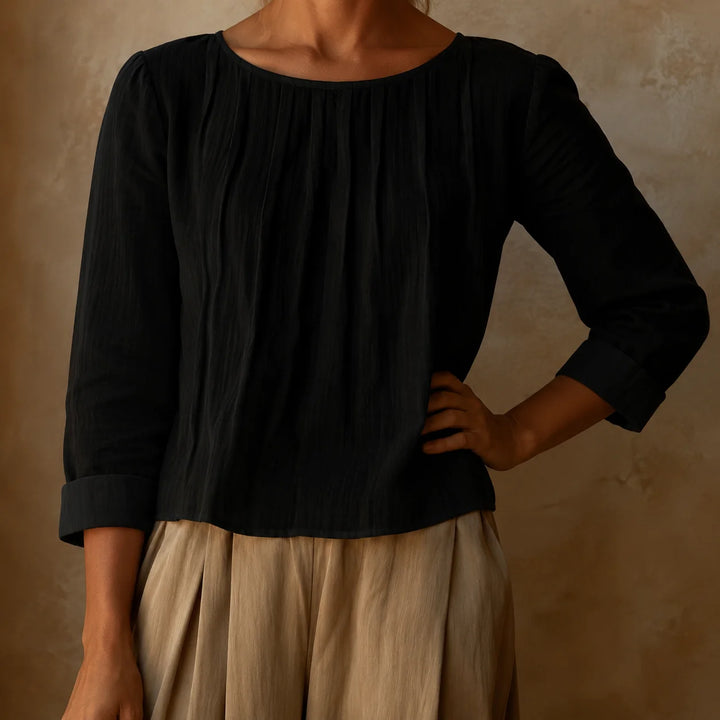 Women's pleated blouse in cream showing lightweight woven fabric texture and soft pleating detail from neckline