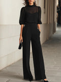 Woman wearing wide leg trousers and sheer blouse set in black with puff sleeves and camisole
