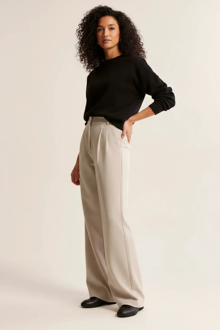 Women's high waist pleated trousers in beige paired with a black jumper for a polished look