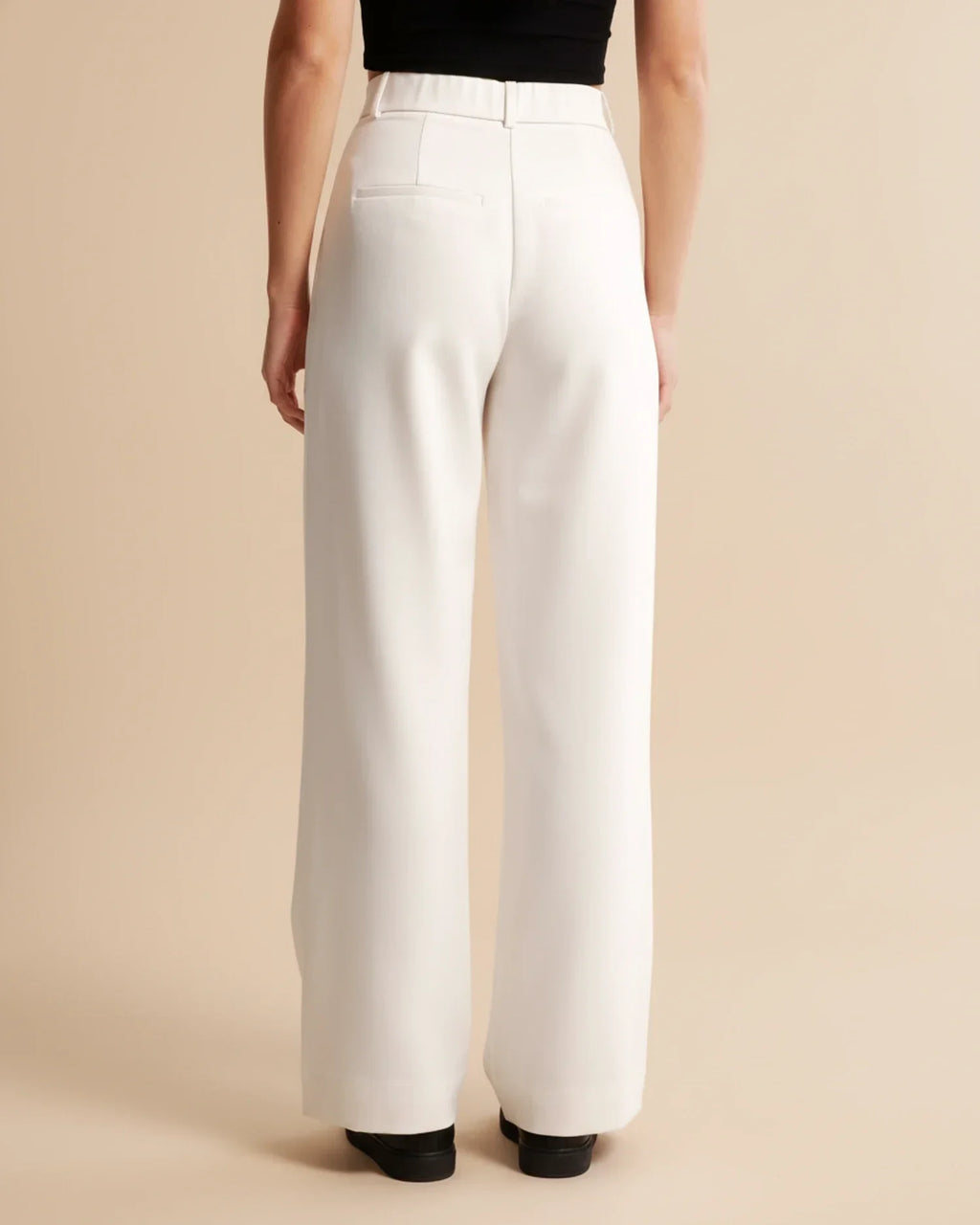 Full-length view of women's high waist pleated trousers in neutral beige tone