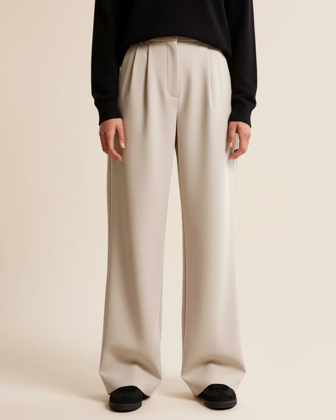 Close-up view of high waist pleated trousers showing tailored front pleats and structured silhouette