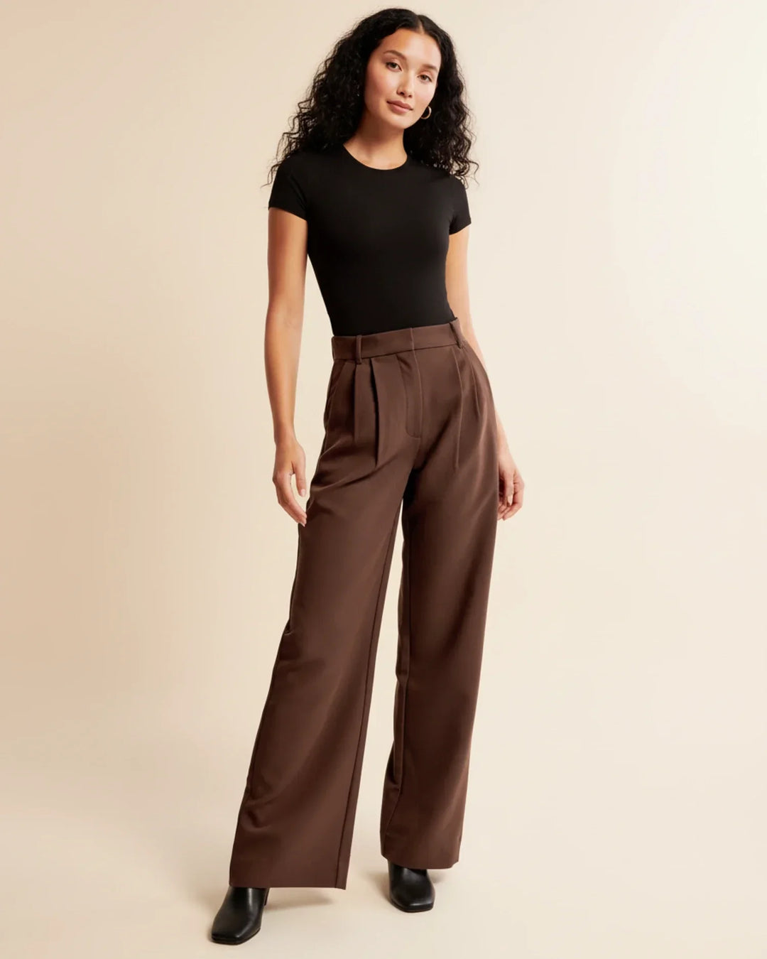 Detail view of tailored pleated trousers showing high-rise waistband and straight leg