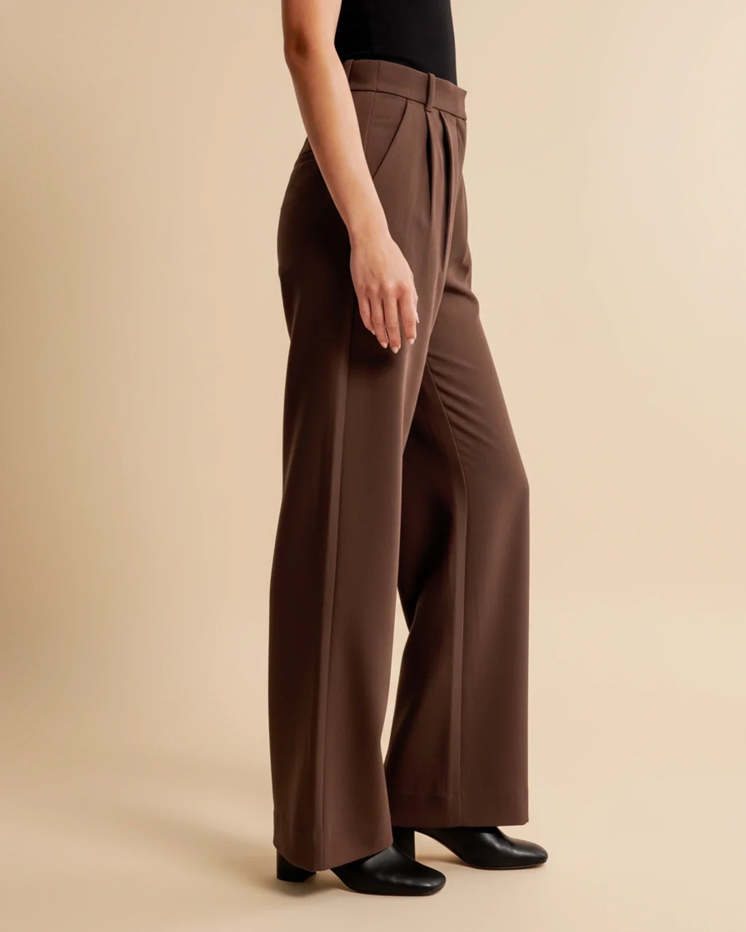 Close-up of high waist pleated trousers showing structured fabric and polished finish