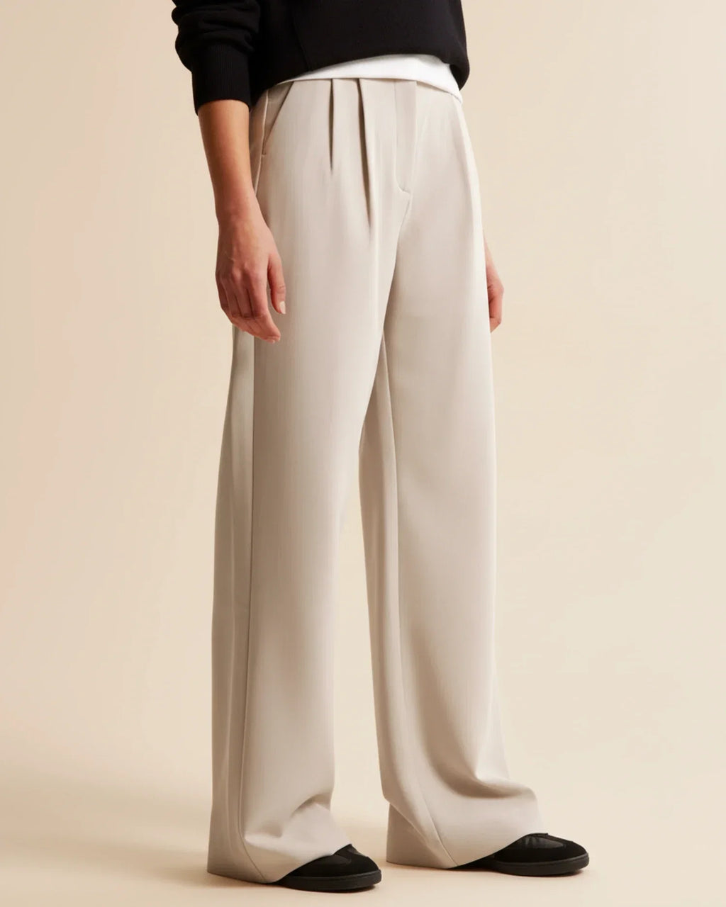 Full-length view of beige high waist pleated trousers styled with black top and shoes