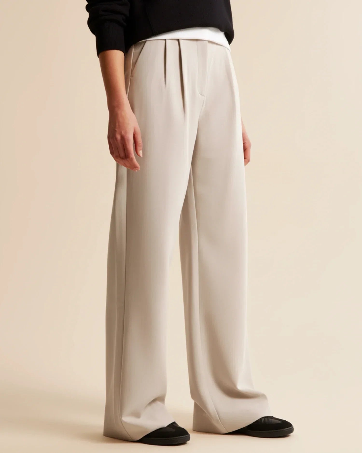 Full-length view of beige high waist pleated trousers styled with black top and shoes
