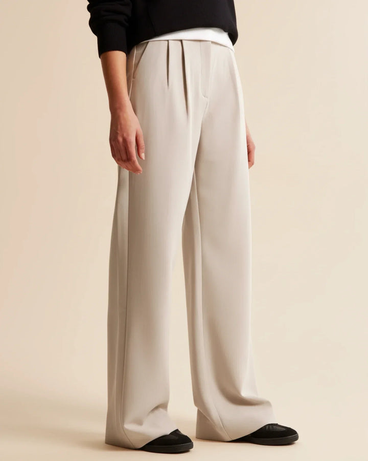 Full-length view of beige high waist pleated trousers styled with black top and shoes