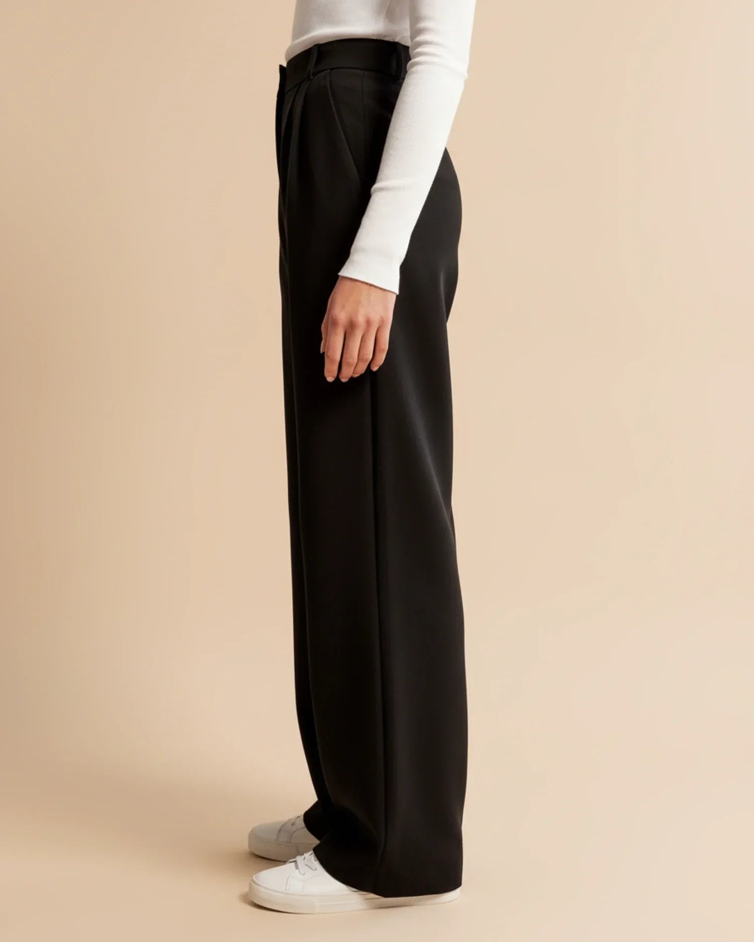 Close-up of pleated trouser waistband showing high-rise fit and structured pleats