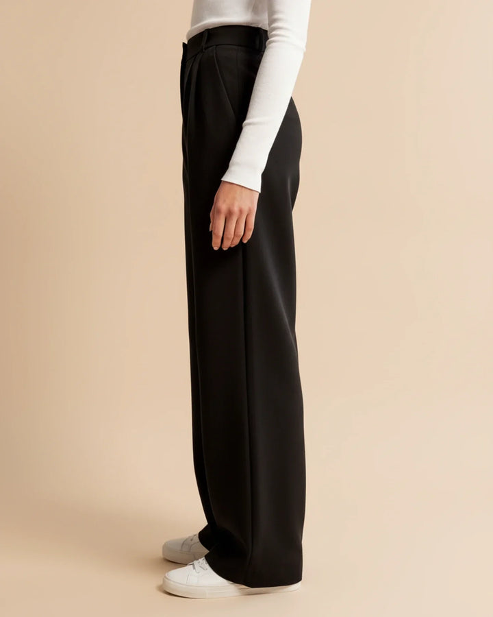 Close-up of pleated trouser waistband showing high-rise fit and structured pleats
