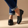 Women's penny loafers in brown paired with cuffed jeans showing slip-on design and structured shape