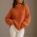 Woman wearing an oversized turtleneck jumper in burnt orange with chunky knit texture and ribbed cuffs