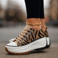 Women's platform trainers with zebra print detailing and chunky white sole, worn with black trousers and gold anklet