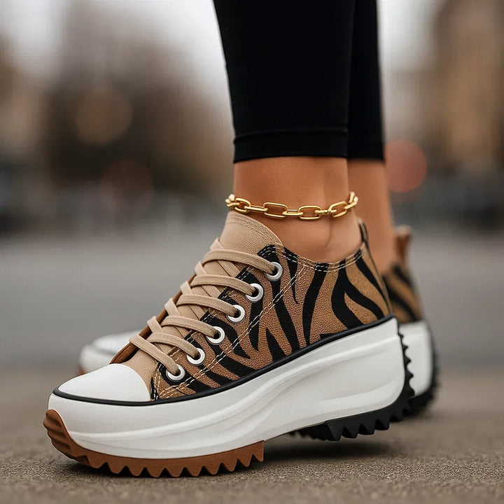 Women's platform trainers with zebra print detailing and chunky white sole, worn with black trousers and gold anklet