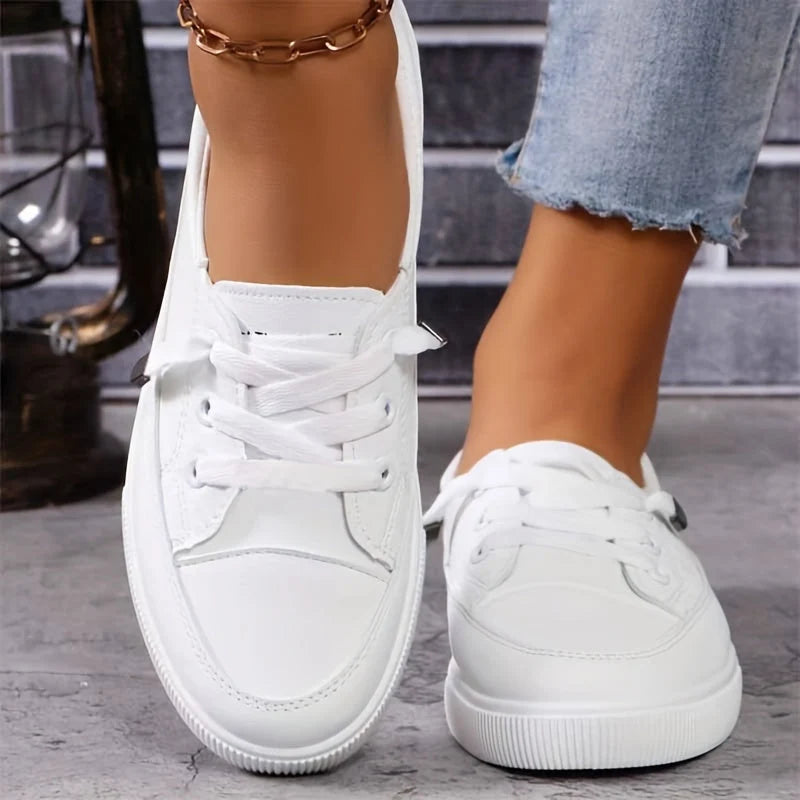 Close-up of white lace-up trainers showing rounded toe and tonal stitching detail on upper