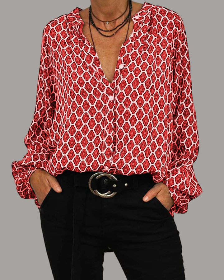 Women's geometric print blouse with long sleeves and ruffle cuffs, worn untucked over black trousers