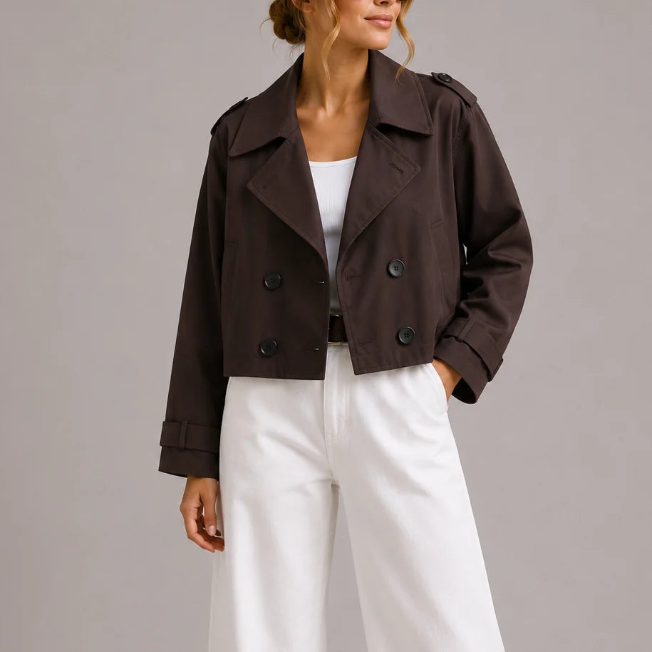 Woman wearing brown cropped trench jacket with double-breasted closure and wide lapels over white trousers